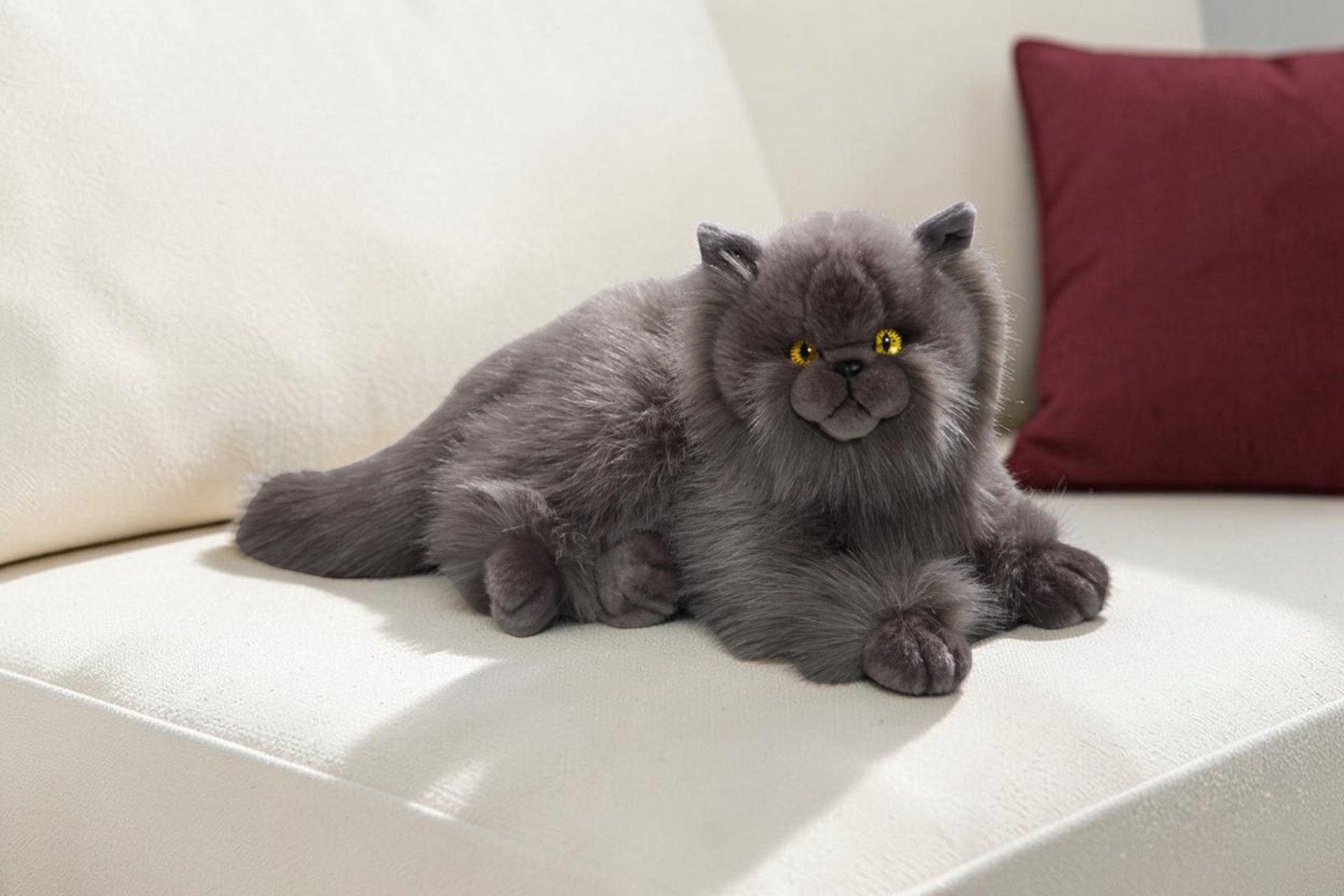 Soft toy cat resting on a light sofa with a red cushion